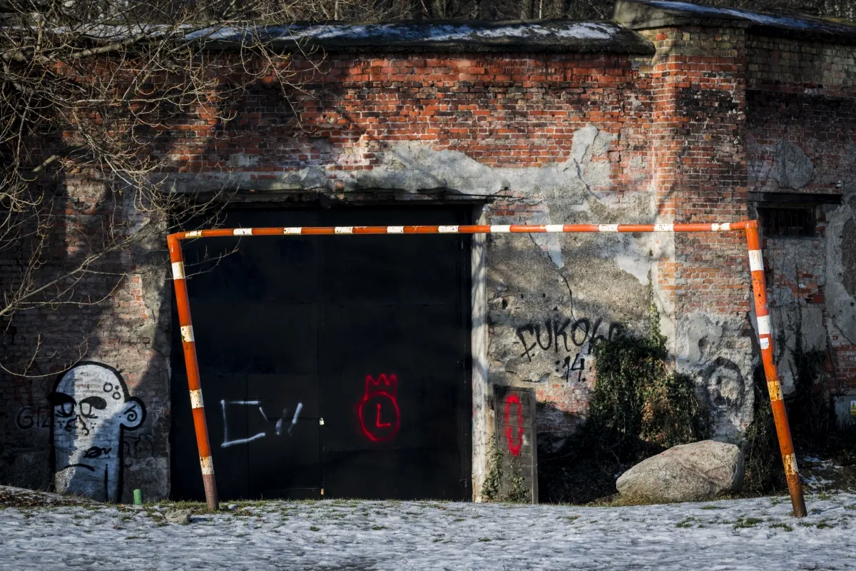 Orange football goal standing in front of a weathered brick wall and black gate